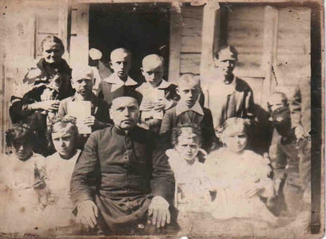 Ks. Henryk Domalewski z dziećmi z Kalonki (Pierwsza Komunia Św., maj lub czerwiec 1938 r.). Zdjęcie wykonane przed domem sołtysa Gocławia, Józefa Piętki. W budynku odbywały się lekcje. Na fotografii: pierwszy rząd od dołu, od lewej strony- Sławomira Osica, Marianna Osica, ks. H. Domalewski, Helena Jałocha. Wanda Krupka; drugi rząd, od lewej-Jan Olszewski, Jan Całka Eugeniusz Zawadka, Czesław Cholewiński. Kobieta po lewej stronie to pani Stefania Możdżonek.